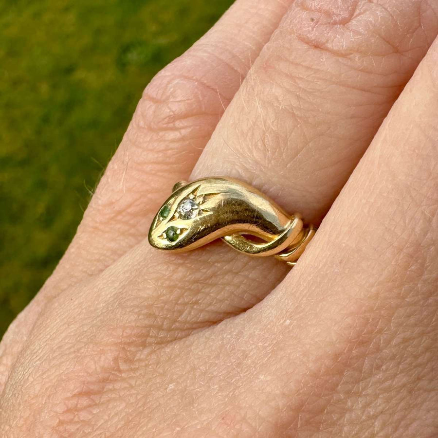Edwardian 18ct gold snake ring featuring diamond and green garnet eyes, coiled elegantly on a finger.