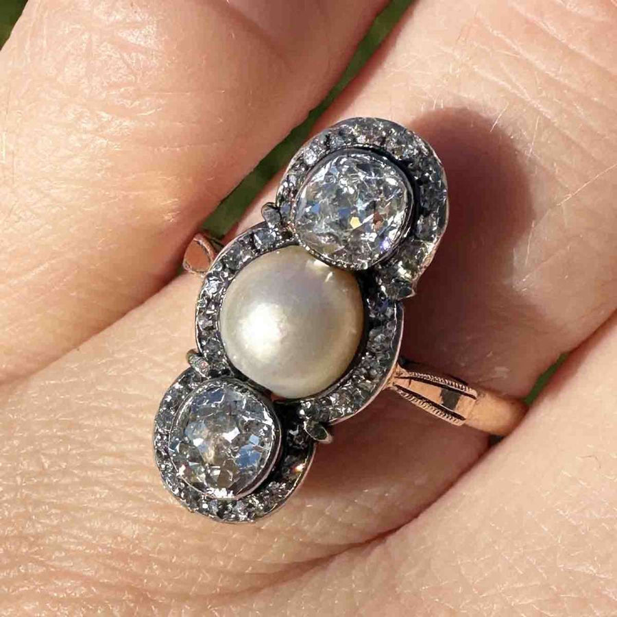 Edwardian silver and gold three stone ring featuring old mine cut diamonds and natural pearl on a hand.